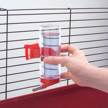 Hand holding a clear water bottle with a red base against a wire cage background